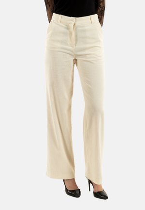 Pantalones de pana ancha color crema con rayas verticales texturizadas, que cuentan con una cintura ajustada, cremallera delantera y bolsillos de lado. Combinados con tacones altos negros.