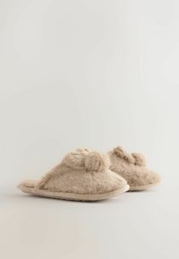 Beige pels-slippers med en blød tekstur, åben tå-design, pom pom-detaljer på forsiden og en neutral farvet sål.