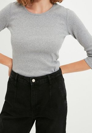 Femme portant un haut ajusté à manches longues côtelé gris clair rentré dans un jean noir taille haute avec fermeture par bouton et fermeture éclair.