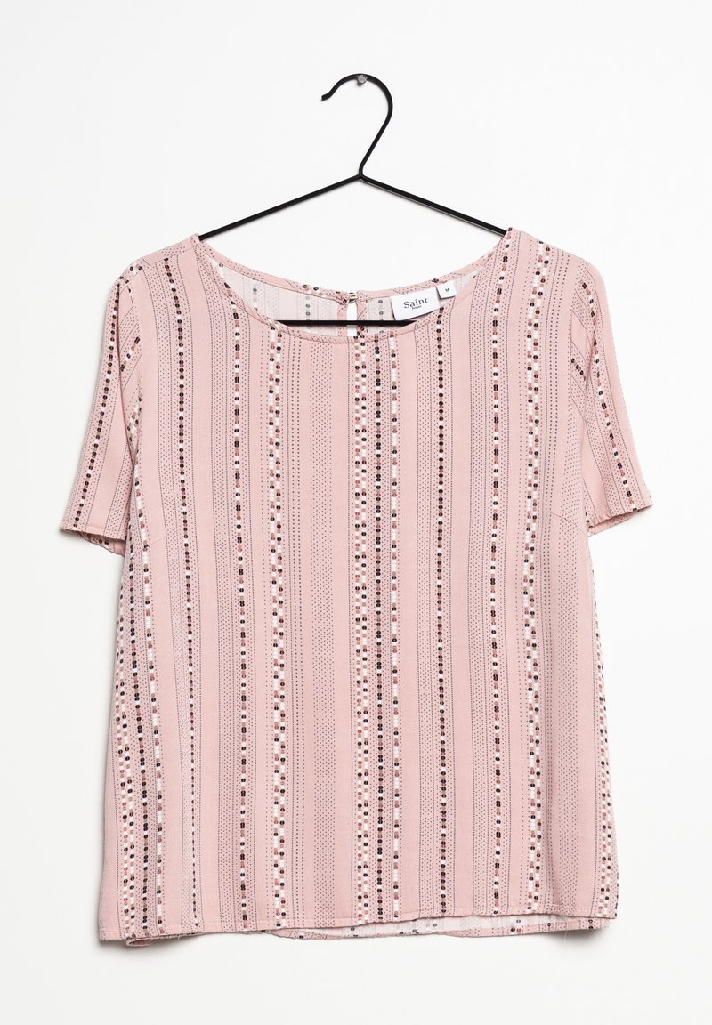 Blouse rose clair à manches courtes avec des rayures verticales en pointillés blanc, noir et marron, suspendue à un cintre en fil noir sur un fond blanc.