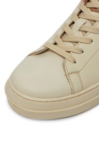 Beige nahkasaapad, millel on sile pind, ümmargune nina, kitsad paelad ja tekstureeritud kummitald. Peen õmbluste detail külgedel.