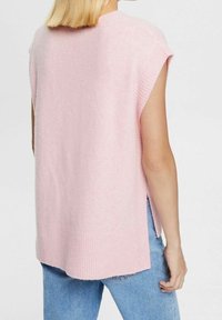 Pull sans manches rose clair avec ourlet côtelé, texture douce, fentes latérales et silhouette décontractée, associé à un jean en denim.