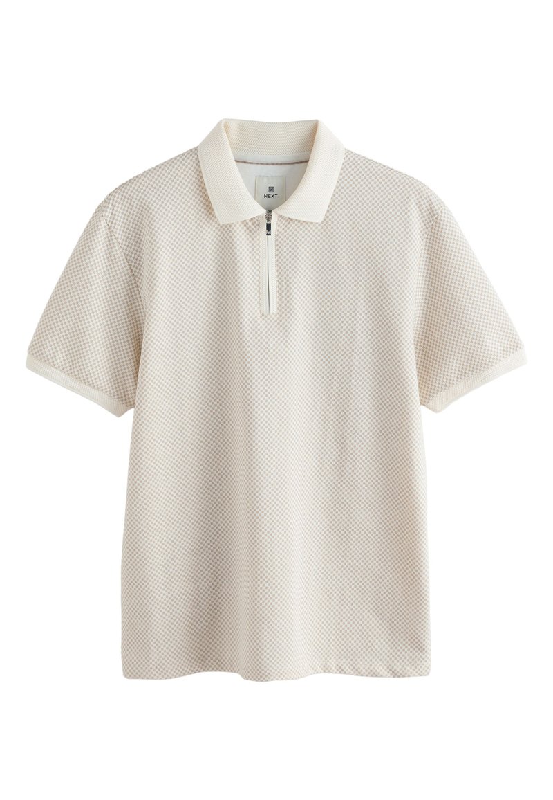 Polo de couleur beige clair avec un motif texturé, manches courtes et une patte de boutonnage zippée à moitié. Tissu en mélange de coton avec un col contrastant.
