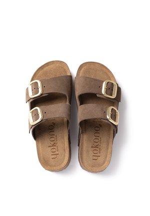 Sandalias de ante marrón con dos hebillas doradas ajustables en cada tira, suela plana y plantilla suave, vistas desde arriba sobre un fondo blanco.