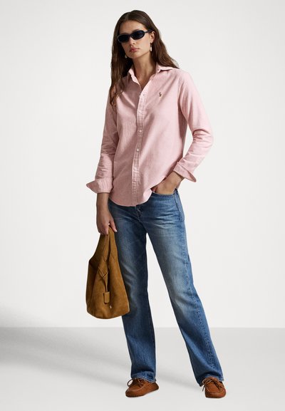 Svetloružová košeľa na gombíky, voľný strih, v kombinácii s modrými džínsami. Doplnky zahŕňajú slnečné okuliare a hnedú semišovú tašku. Obuvou sú hnedé mokasíny.