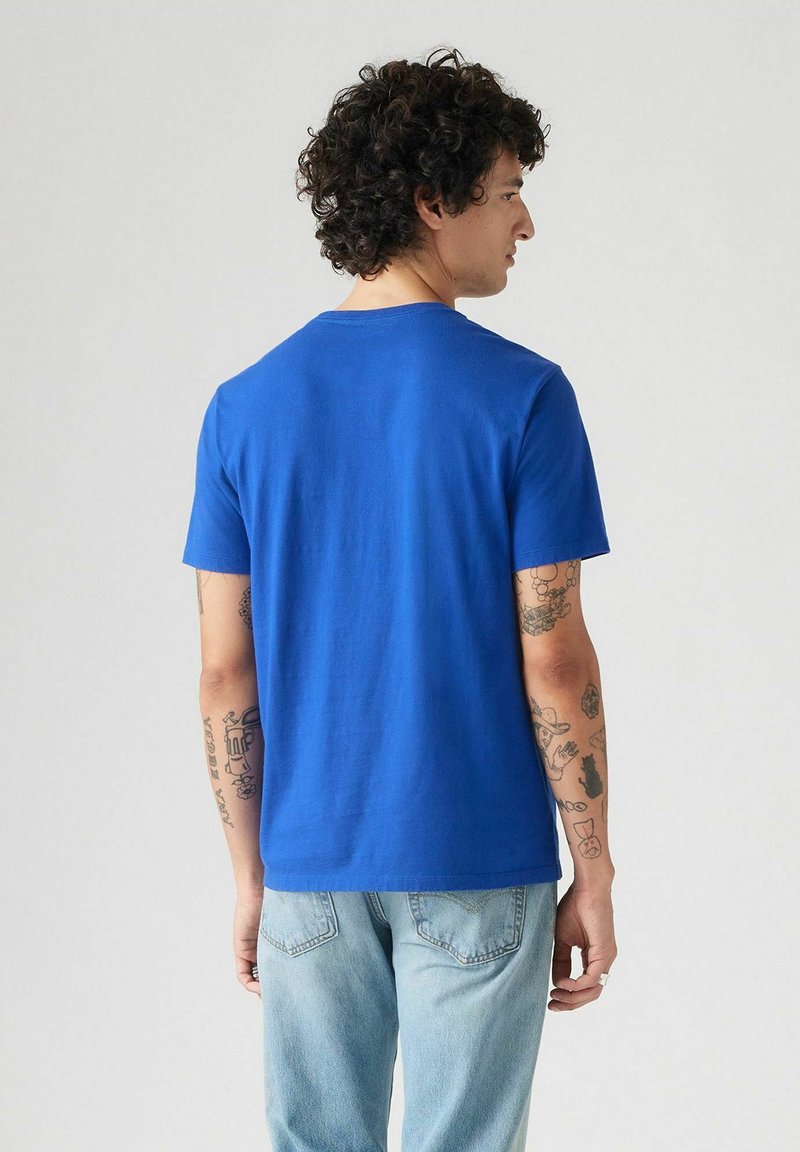 Camiseta de algodón azul con mangas cortas, escote redondeado y corte relajado, combinada con vaqueros de mezclilla azul claro.