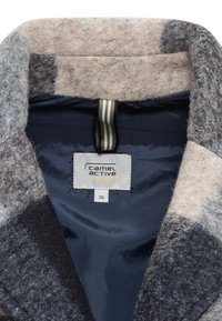 Wollen blazer met een grijs en beige gemêleerde buitenkant, marineblauwe voering en een ophanglus. Voorzien van een label met merk- en maatgegevens.