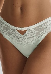Muntgroene kantondergoed met bloemmotieven, golvende randen en een klein strikje in het midden voor boven een doorschijnend kantpaneel.