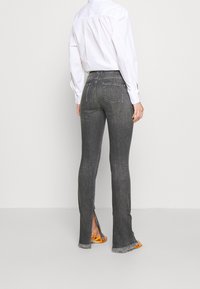 Gray denim flared jeans with side slits, frayed hems, and contrasting stitching. Paired with a white shirt and orange sandals.
