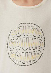 Crème-kleurig t-shirt gemaakt van zachte katoen. Heeft een cirkelvormige grafiek met vetgedrukt, overlappend "SOUND"-tekst in zwart en geel. Ronde hals ontwerp.