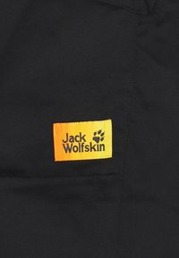 Černá tkanina s žlutou a oranžovou nálepkou s nápisem "Jack Wolfskin" a designem otisku tlapy, našitá do materiálu.