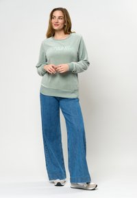 Ljusgrön sweatshirt med präglad text, kombinerad med vida blå jeans. Inkluderar ribbade ärmslut och en mjuk, texturerad finish.