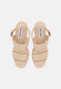 Beige hæle sandaler med to vævede stropper, en struktureret sål og en lukning med spænde på siden. Glat finish og firkantet tå design.