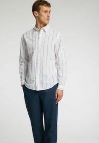 Vit långärmad skjorta med blå vertikala ränder, knappar fram, tillsammans med marinblå byxor. Slät tyg, klassisk kragsdesign.