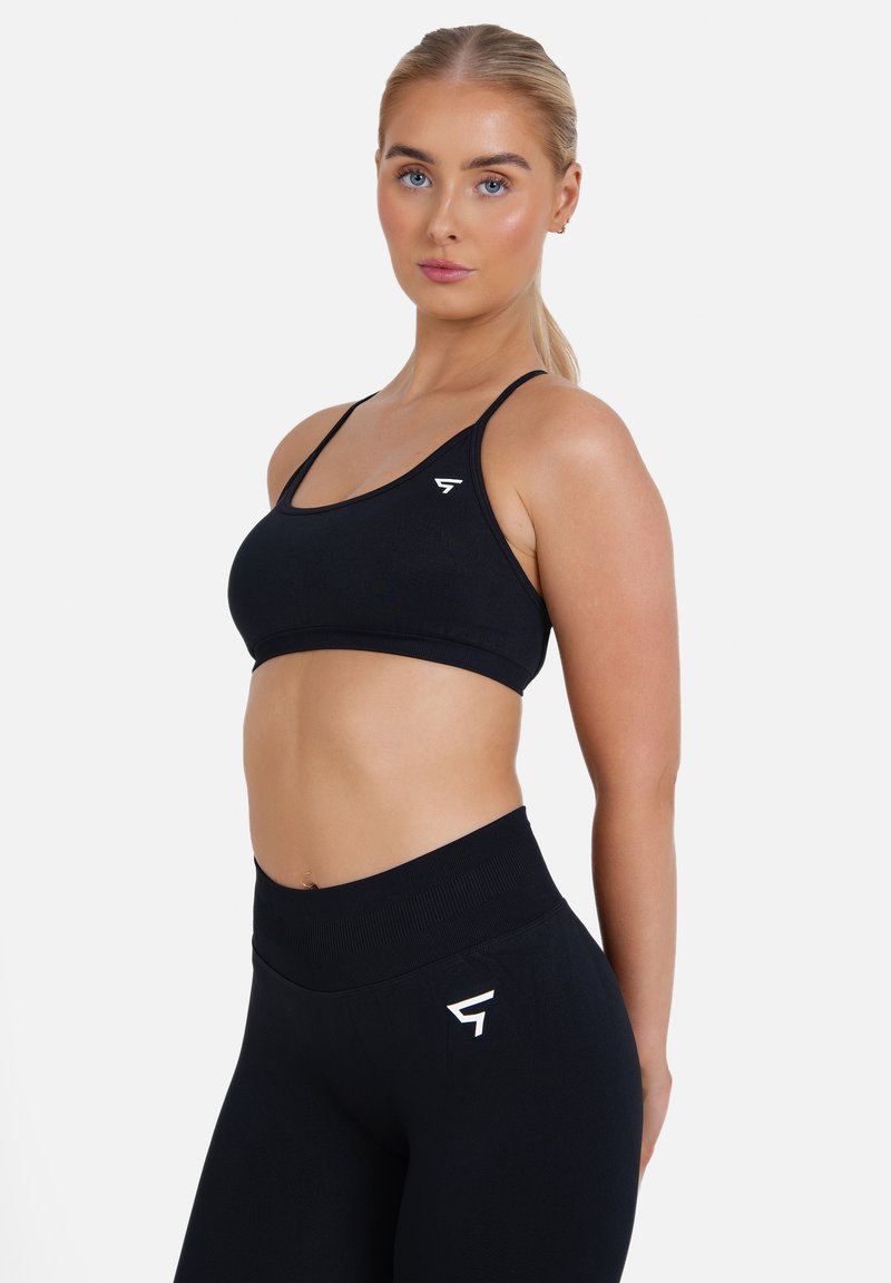 Top sportivo nero dal design aderente con spalline sottili, abbinato a leggings neri a vita alta con un piccolo logo bianco sull'anca.