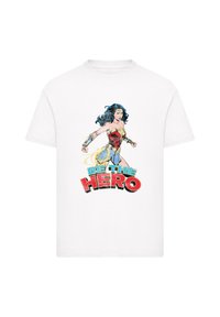 White cotton t-shirt featuring a colorful Wonder Woman graphic with the text "BE THE HERO" in bold red and blue. Short sleeves and crew neck.