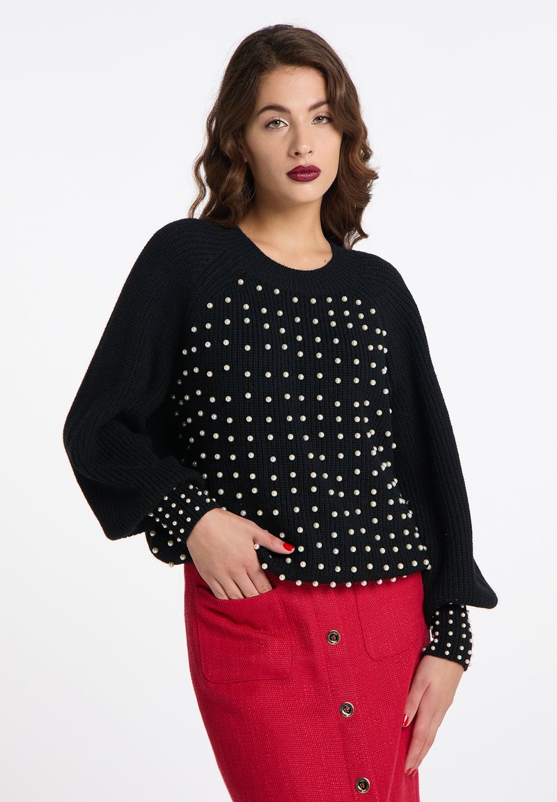 Maglione nero lavorato a maglia con motivo testurizzato e decorazioni in perle su corpo e maniche, abbinato a una gonna rossa con bottoni frontali.