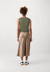Grønn teksturert ermeløs topp kombinert med en beige satin midi skjørt, som har en glatt overflate, og hvite joggesko med grønne detaljer.