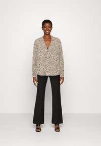 Top com padrão de leopardo em bege e castanho, design de decote em V com mangas longas, combinado com calças pretas largas e sandálias pretas de tiras.