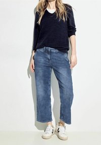 Suéter navy con escote en V, jeans de pierna ancha de color azul claro y zapatillas blancas con acentos negros. Textura suave y corte holgado.