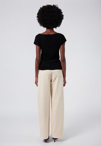 Top de punto negro de manga corta con un diseño texturizado, combinado con pantalones anchos crema que presentan un detalle de bolsillo en la parte trasera.