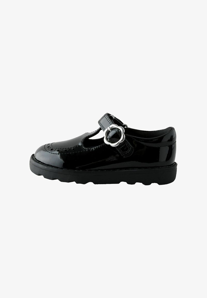 Chaussure Mary Jane noire brillante avec boucle argentée en forme de fleur, semelle épaisse et perforations décoratives dans la zone des orteils.