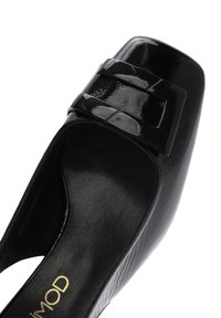 Black patent leather slip-on shoe with a square toe, featuring a pronounced glossy bow accent and a textured inner lining.