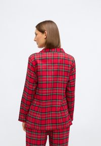 Rødternet jakke med krave, lange ærmer og lommer. Stoffet har et tartanmønster med sorte og grønne accenter og en blød tekstur.