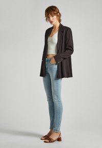 Americana negra, top corto blanco con textura, jeans ajustados de color azul claro y sandalias de tacón cuadrado marrones con tiras. La americana tiene botones plateados.