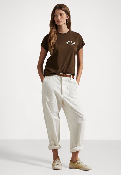 Brązowy t-shirt z krótkim rękawem z logo "POLO", w połączeniu z zwiniętymi białymi luźnymi spodniami i casualowymi beżowymi sneakersami. Subtelny detal paska.