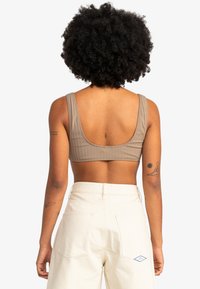 Light brown ribbed bralette with wide straps, displayed from the back, paired with high-waisted cream pants featuring back pockets.
