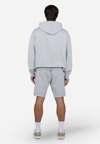 Sudadera gris claro con capucha y puños acanalados, combinada con un pantalón corto a juego. Tela suave y texturizada con un corte relajado.