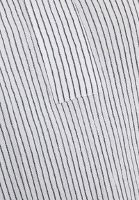 Tessuto bianco con sottili righe verticali nere, dotato di una tasca sul lato sinistro. La texture sembra morbida e leggera.