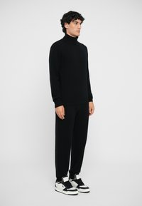Schwarzer Rollkragenpullover kombiniert mit lässigen schwarzen Hosen und schwarz-weißen Sportschuhen, mit weicher Textur und minimalistischem Design.