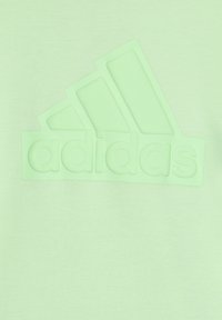 Sudadera verde claro con un logo de Adidas en relieve y mate del mismo color. Textura suave con un fondo liso, sin patrones ni acentos.