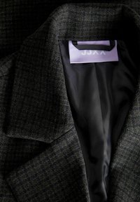Blazer grigio scuro con tessuto testurizzato, revers a punta e foderatura nera liscia. L'etichetta riporta "JJXX."