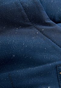 Tissu imperméable bleu marine avec une texture matelassée, présentant des gouttelettes d'eau à la surface, mettant en avant ses propriétés hydrofuges.