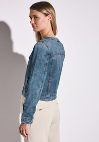 Denimjacka i ljusblått; figursydd design med långa ärmar, ryggsöm och framfickor. Slät textur med kontrasterande sömmar.