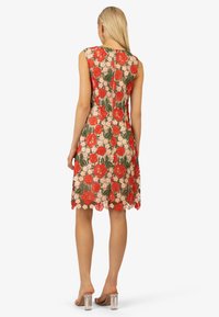 Abito in pizzo floreale con ricami di rose rosse e margherite bianche, design senza maniche, orlo a scallop e chiusura con zip posteriore. Tacchi a blocco trasparenti visibili.