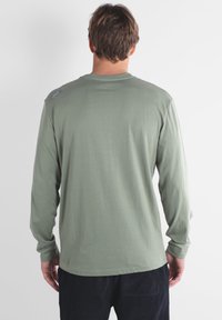 Chemise à manches longues en coton vert olive doux, avec un col rond et des détails de couture subtils au dos. Texture lisse sur l'ensemble.
