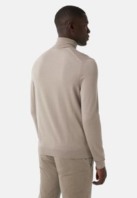 Un pull à col roulé beige en tissu tricoté lisse, avec des manches longues et une silhouette ajustée, doté de bords côtes aux poignets et à l'ourlet.