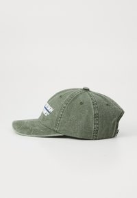 Olive green baseball cap with stitched ventilation holes and embroidered white and blue text on the front.