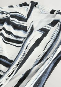 Blouse en noir et blanc, avec un tissu fluide orné de rayures verticales de différentes largeurs et nuances de bleu, formant un motif ondulant.