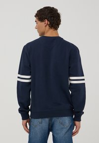 Granatowa bluza z okrągłym dekoltem i długimi rękawami, z białymi poziomymi paskami na każdym rękawie i miękką teksturą.