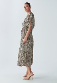 Maxi kleita ar krēmkrāsas un melnas zebradrukas rakstu, īsām piedurknēm, pieguļošu vidukli un plats kāju siluets. Valkāta kopā ar bēša toņa augstpapēžu kurpēm.