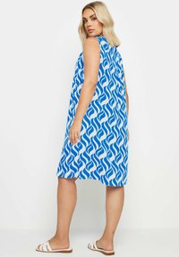 Sininen ja valkoinen olkaimeton mekko, jossa on aalto kuvio, löysä siluetti, pyöreä pääntie ja polvimittainen helma. Yhdistetty valkoisten sandaalien kanssa.