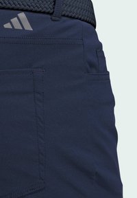 Mornarsko plave kratke hlače s vidljivim šavovima, bočnim džepom i teksturiranim tkanim remenom. Na džepu se nalaze sivi Adidas logotip.