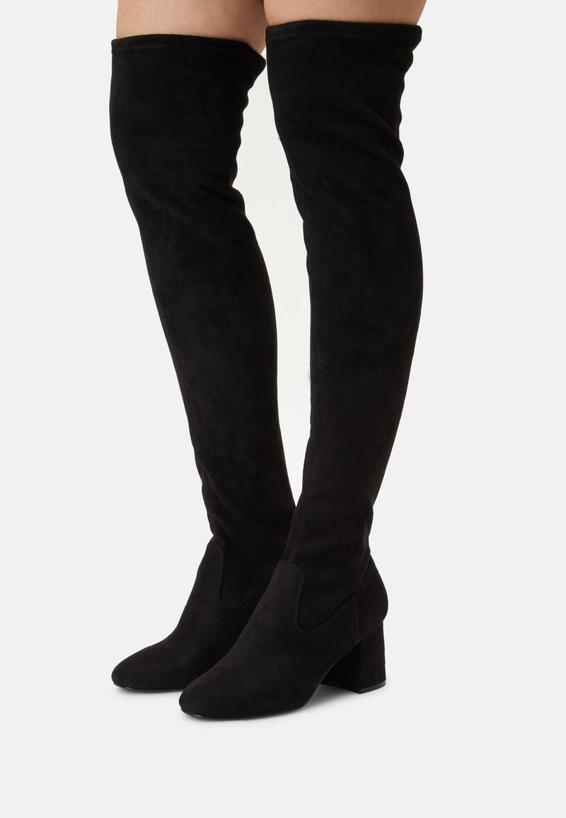 Botas de ante negras por encima de la rodilla con un tacón grueso y textura suave. Presenta puntera redondeada y detalle en los paneles laterales para un diseño adicional.