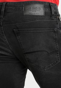 Vaqueros de mezclilla negra con una textura suave y un brillo sutil. Cuenta con un bolsillo trasero con detalles de costura y una etiqueta de cuero de Mavi Jeans Co.