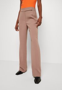 Beige skräddarsydda byxor med hög midja, utsvängda ben och en slät textur, kombinerade med svarta spetsiga skor.